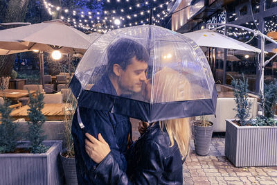 Romantic couple man and woman under an umbrella in the rain on the background of a street cafe.