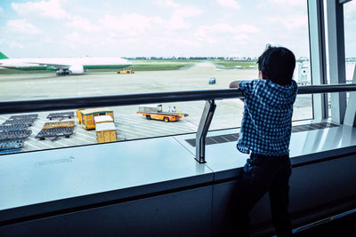 Rear view of boy standing by railing at airport