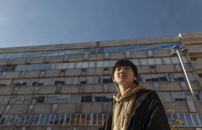 Asian teenage boy with earphones against building on street. madrid. spain