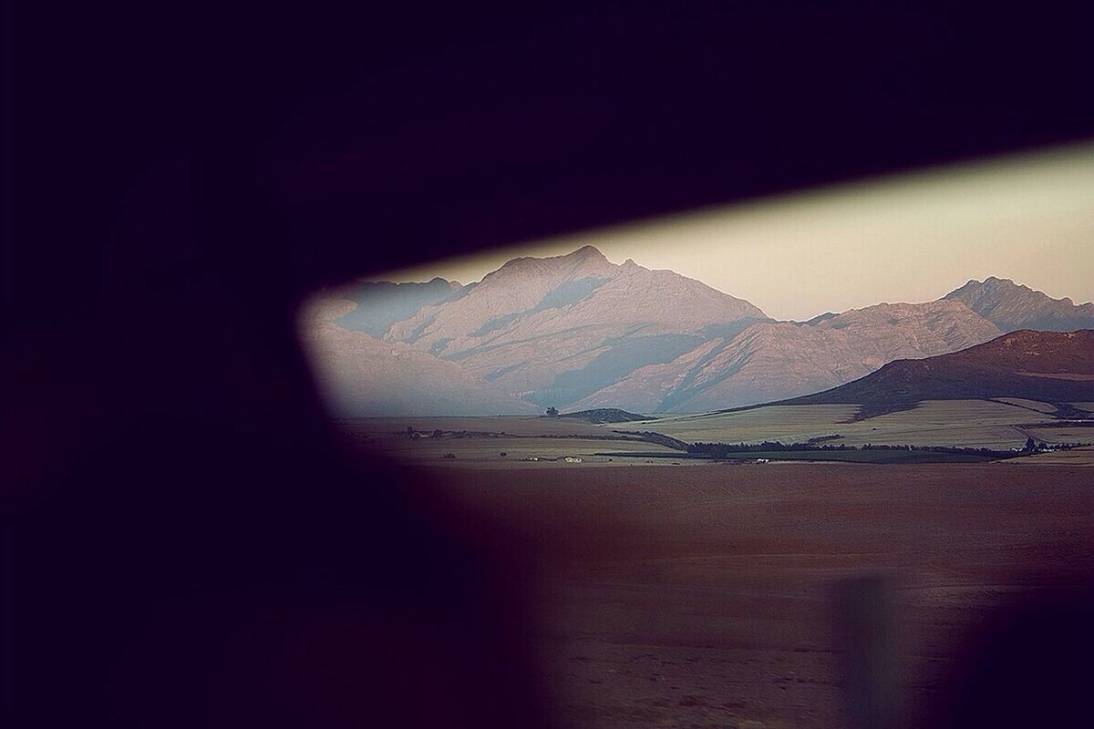 indoors, window, sea, water, mountain, beach, tranquility, scenics, tranquil scene, beauty in nature, sunlight, sky, nature, horizon over water, silhouette, curtain, transparent, home interior, copy space, sand