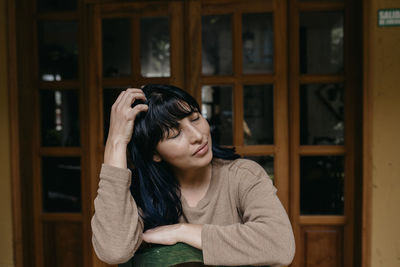 Portrait of young woman looking through window at home