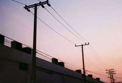 Low angle view of silhouette electricity pylon and building against sky