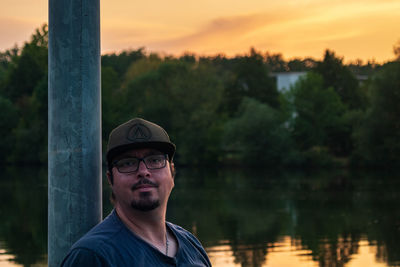Portrait of young man standing against lake during sunset