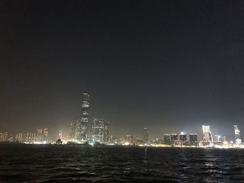 Illuminated cityscape by sea against clear sky at night