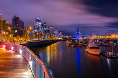 Illuminated city by river against sky at night