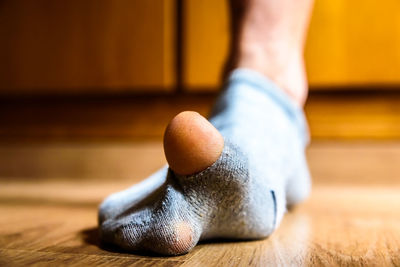 Low section of man wearing torn sock on wooden floor