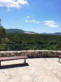 Empty bench on countryside landscape against blue sky