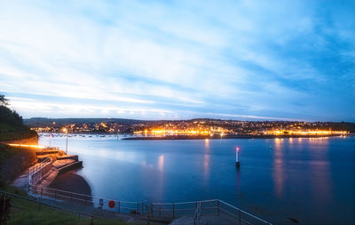 Illuminated city by sea against sky at night