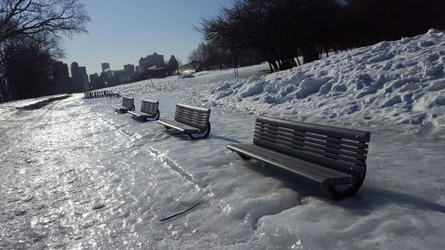 Empty bench on snow covered field against sky