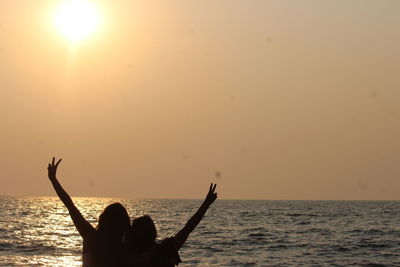 Friends gesturing peace sign at beach against sky during sunset