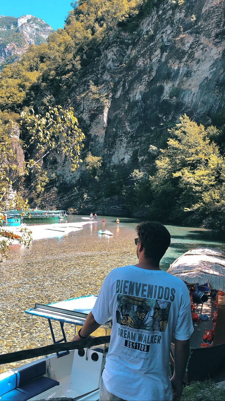 REAR VIEW OF YOUNG MAN LOOKING AT VIEW OF MOUNTAIN