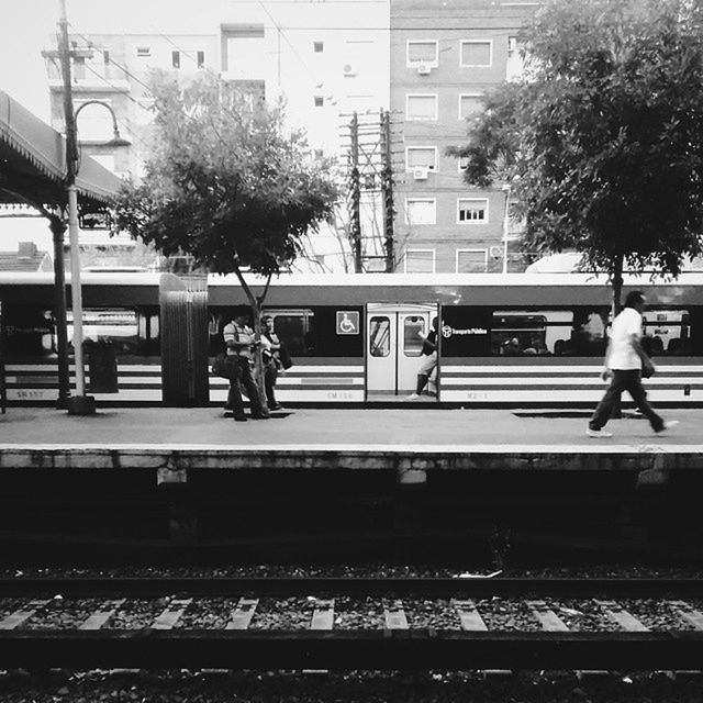 architecture, building exterior, built structure, city, transportation, tree, railroad track, men, city life, railroad station platform, person, public transportation, railroad station, walking, rail transportation, mode of transport, incidental people, lifestyles, railing