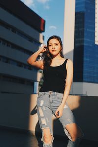 Young woman wearing torn jeans looking away standing against building on terrace 