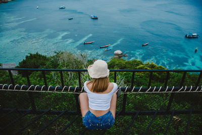 Rear view of woman sitting on railing by sea