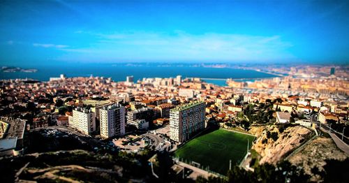 High angle view of cityscape by sea against blue sky