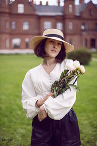 Portrait of a beautiful young woman in a hat , holding a bouquet of peonies in her hands.