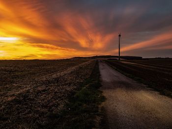 Dirt road amidst field against sky during sunset