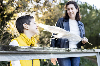 Mother tickling son with feather by railing in park