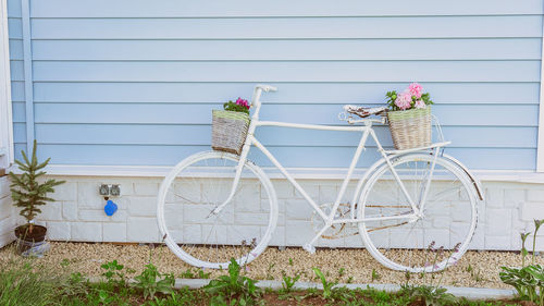 Retro bicycle with two baskets of flowers on the background of a blue house. garden decor 