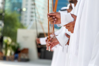 Midsection of man holding umbrella standing against white wall