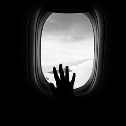 Silhouette man against sky seen through airplane window