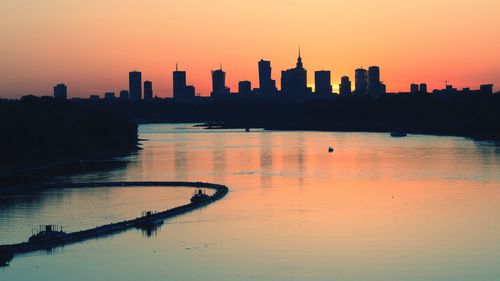 Scenic view of river by silhouette buildings during sunset