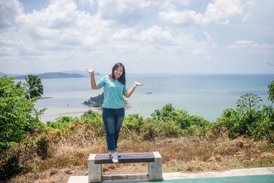 Portrait of smiling woman standing on seat against sea