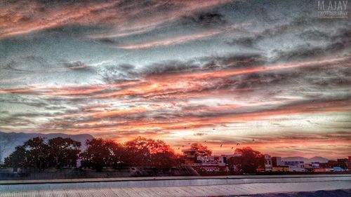 Illuminated cityscape against dramatic sky at sunset