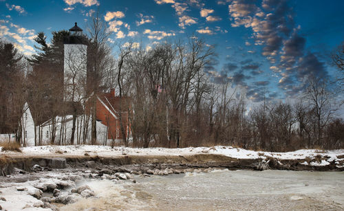 Bare trees on snow covered field against sky