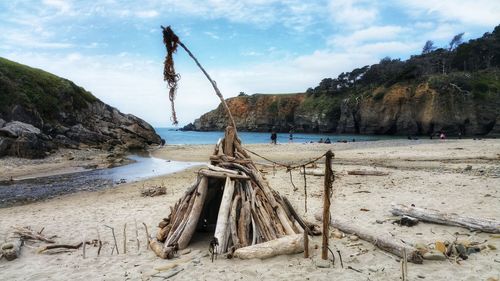 Scenic view of driftwood teepee on ocean beach against sky