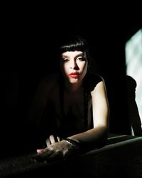 Portrait of beautiful young woman sitting against black background