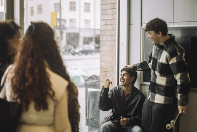 Happy teenage boy laughing with male and female friends near glass window