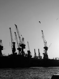 Silhouette cranes at harbor against clear sky