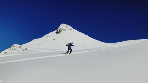 Low angle view of man skiing on snowcapped mountain against clear blue sky