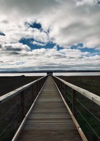 Footbridge leading towards wooden bridge against sky