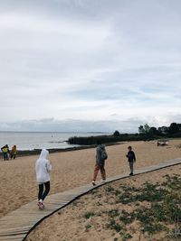 Rear view of couple walking on beach against sky