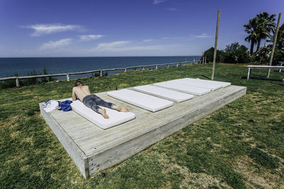 Man lying on mattress against sea and sky