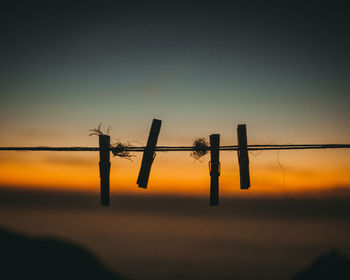 Silhouette clothespins on clothesline against sky during sunset