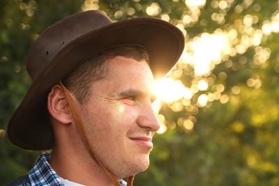 Young man farmer in cowboy hat at agricultural field on green blurred background. closeup portrait 