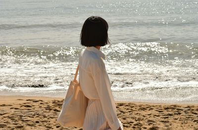 Side view of young woman standing at beach during sunny day