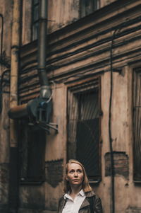 Portrait of young woman standing against building