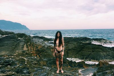 Woman standing on rock by sea against sky