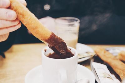 Cropped image of person dipping churro in chocolate at table