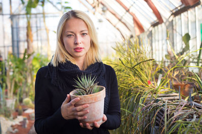 Portrait of woman holding potted plant in greenhouse