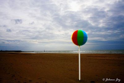 Multi colored balloons on beach against sky