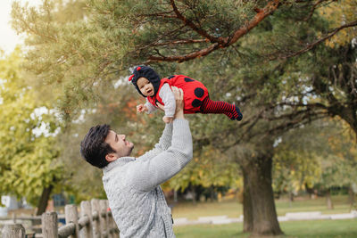 Side view of father carrying daughter in mid-air at park