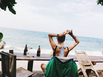 Woman sitting on table at beach against sky