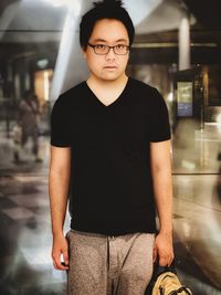 Young asian man in eyeglasses standing against reflective illuminated background.