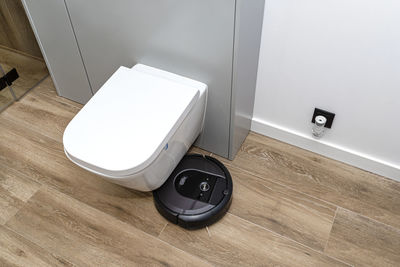 A modern robotic vacuum cleaner cleans the ceramic tiles in the bathroom next to the toilet. 