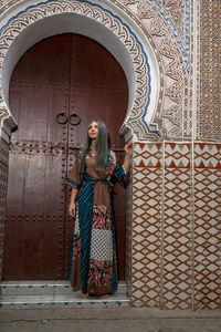 Woman looking away while standing against door of building